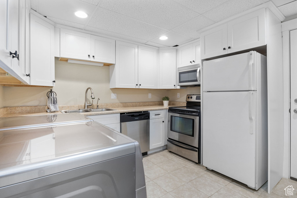 Kitchen with sink, stainless steel appliances, light tile patterned floors, washer / clothes dryer, and white cabinets