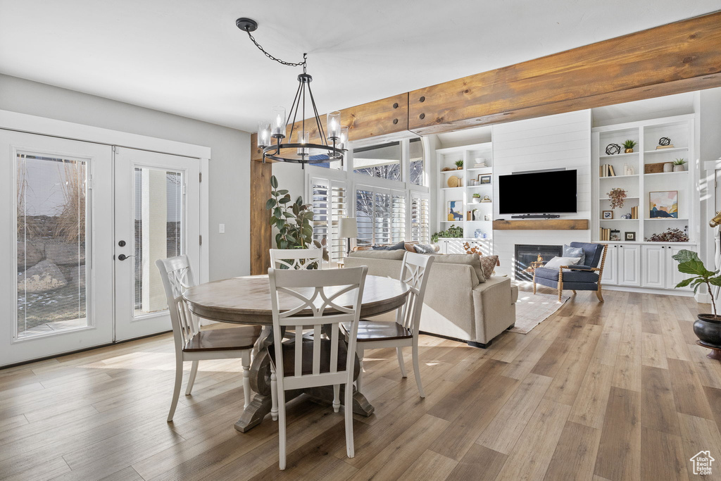 Dining room with a large fireplace, an inviting chandelier, french doors, and hardwood / wood-style flooring