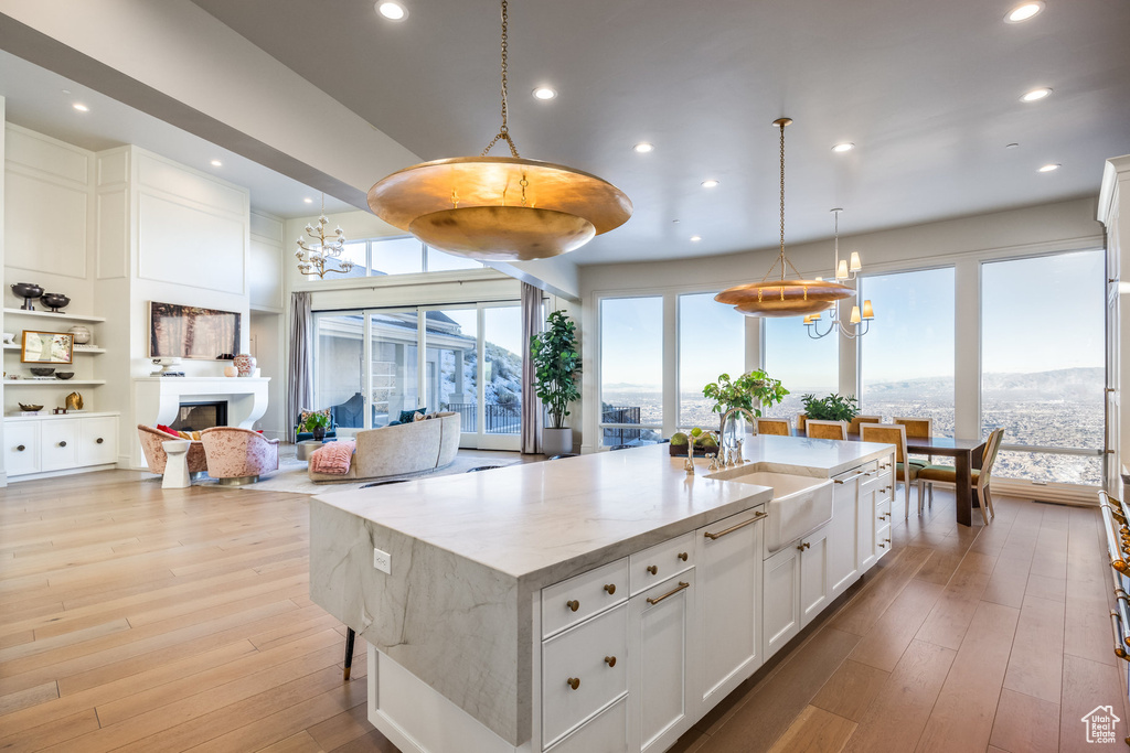 Kitchen featuring a center island with sink, white cabinets, pendant lighting, and light wood-type flooring