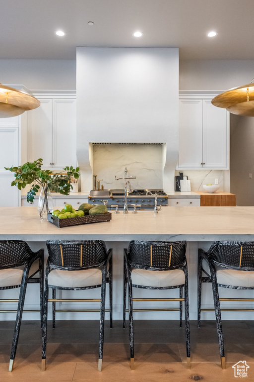 Kitchen featuring white cabinetry, recessed lighting, light countertops, a breakfast bar, and tasteful backsplash