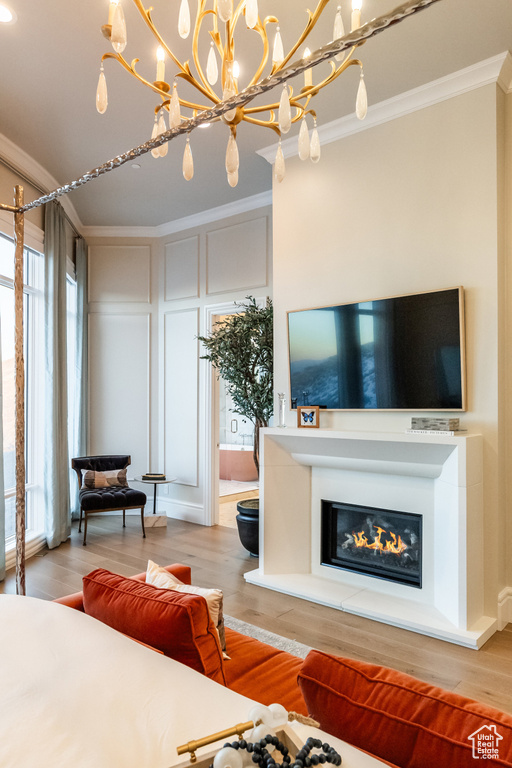 Living room with ornamental molding, wood finished floors, a glass covered fireplace, a chandelier, and a decorative wall