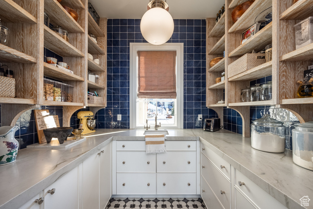 Kitchen featuring decorative backsplash, white cabinetry, sink, and tile walls