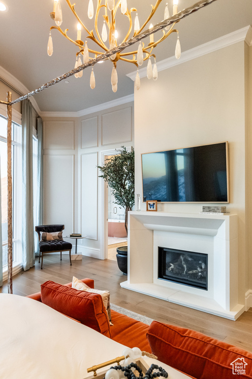 Living room featuring crown molding, wood finished floors, a glass covered fireplace, a chandelier, and a decorative wall
