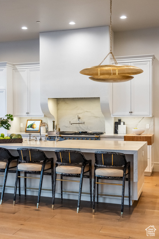 Kitchen with white cabinetry, a kitchen breakfast bar, light countertops, recessed lighting, and light wood finished floors
