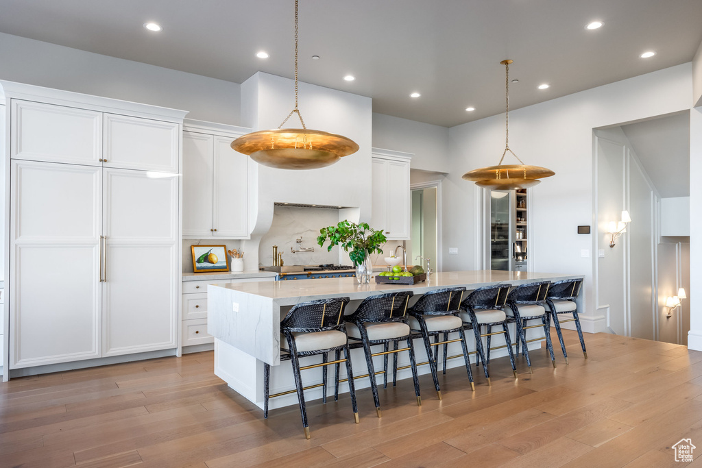 Kitchen with a spacious island, white cabinets, light wood-type flooring, a breakfast bar area, and recessed lighting