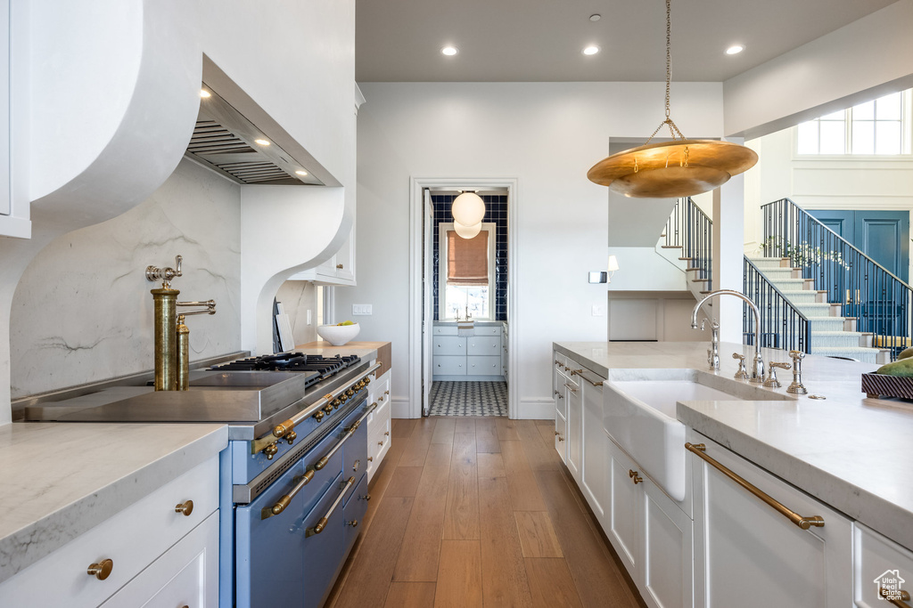 Kitchen with white cabinetry, sink, hanging light fixtures, wall chimney range hood, and dark hardwood / wood-style floors