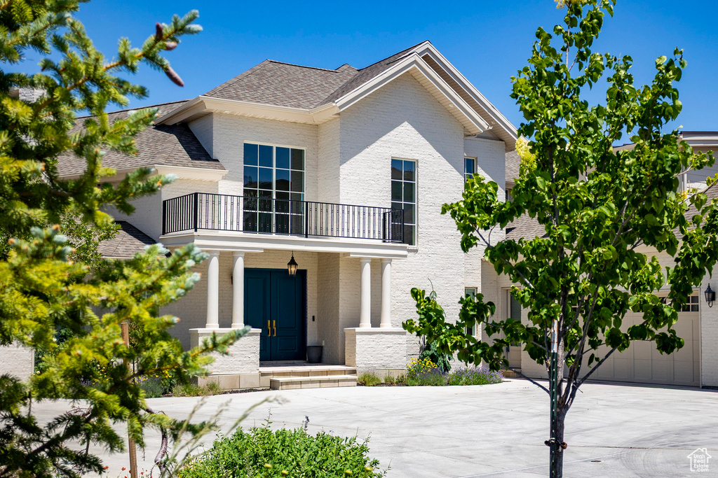 View of front of house featuring a balcony, brick siding, driveway, and a shingled roof