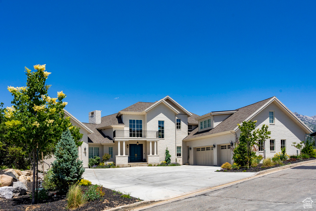 View of front of home featuring concrete driveway, a balcony, a chimney, and a shingled roof
