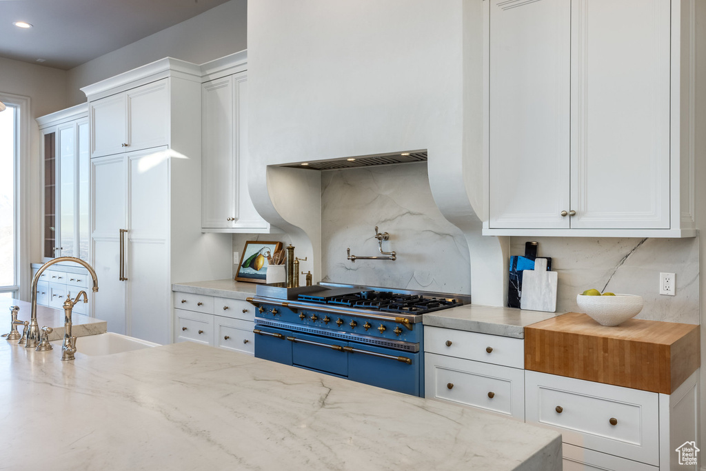 Kitchen featuring stainless steel range, white cabinetry, sink, and light stone countertops