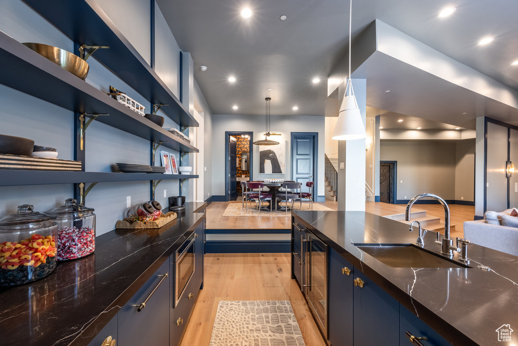 Kitchen featuring light wood-style floors, stainless steel microwave, open floor plan, dark stone countertops, and recessed lighting