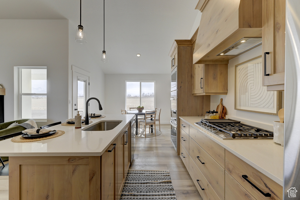 Kitchen with appliances with stainless steel finishes, light brown cabinetry, decorative light fixtures, sink, and a center island with sink