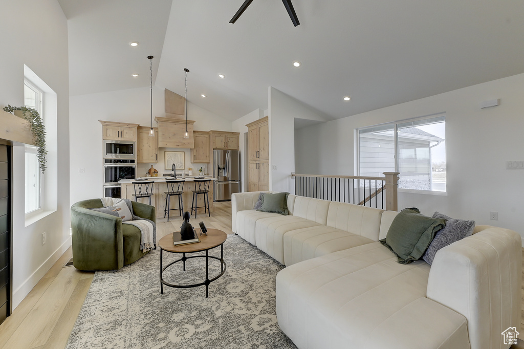 Living room with ceiling fan, high vaulted ceiling, sink, and light wood-type flooring