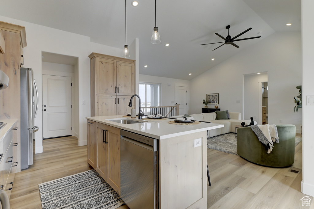 Kitchen with light brown cabinetry, decorative light fixtures, sink, stainless steel appliances, and a center island with sink