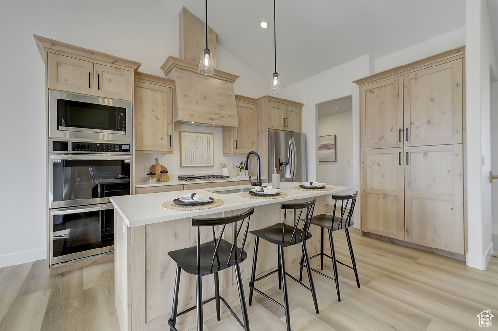 Kitchen featuring stainless steel appliances, hanging light fixtures, and light brown cabinetry