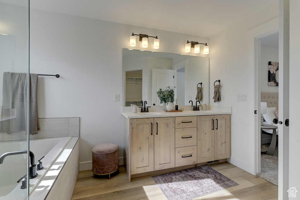 Bathroom featuring vanity, tiled tub, and wood-type flooring