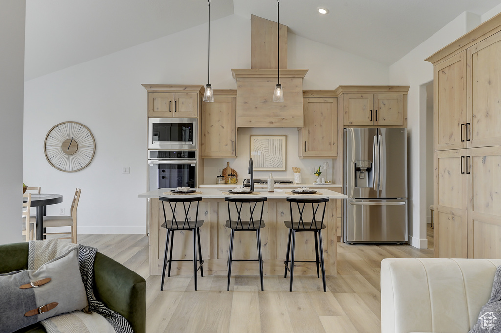 Kitchen featuring decorative light fixtures, a breakfast bar area, light brown cabinets, and appliances with stainless steel finishes