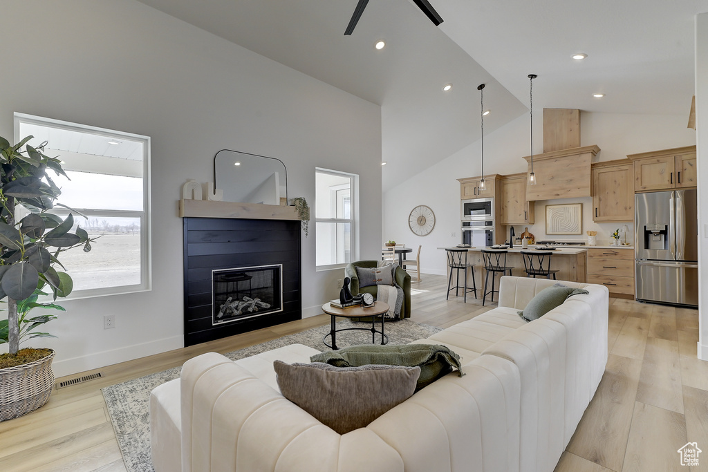 Living room with ceiling fan, plenty of natural light, light hardwood / wood-style floors, and high vaulted ceiling