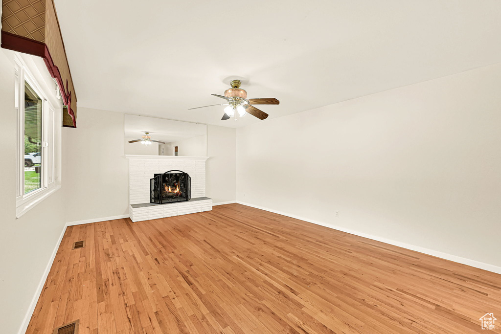Unfurnished living room with a fireplace, baseboards, light wood-style floors, and a ceiling fan