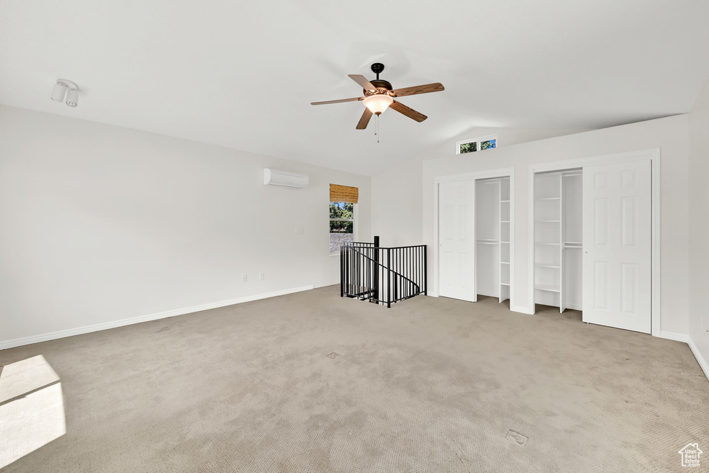 Unfurnished bedroom featuring multiple closets, lofted ceiling, a wall mounted AC, carpet, and baseboards