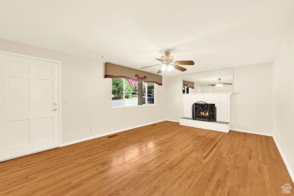 Unfurnished living room with light wood finished floors, a brick fireplace, a ceiling fan, and baseboards