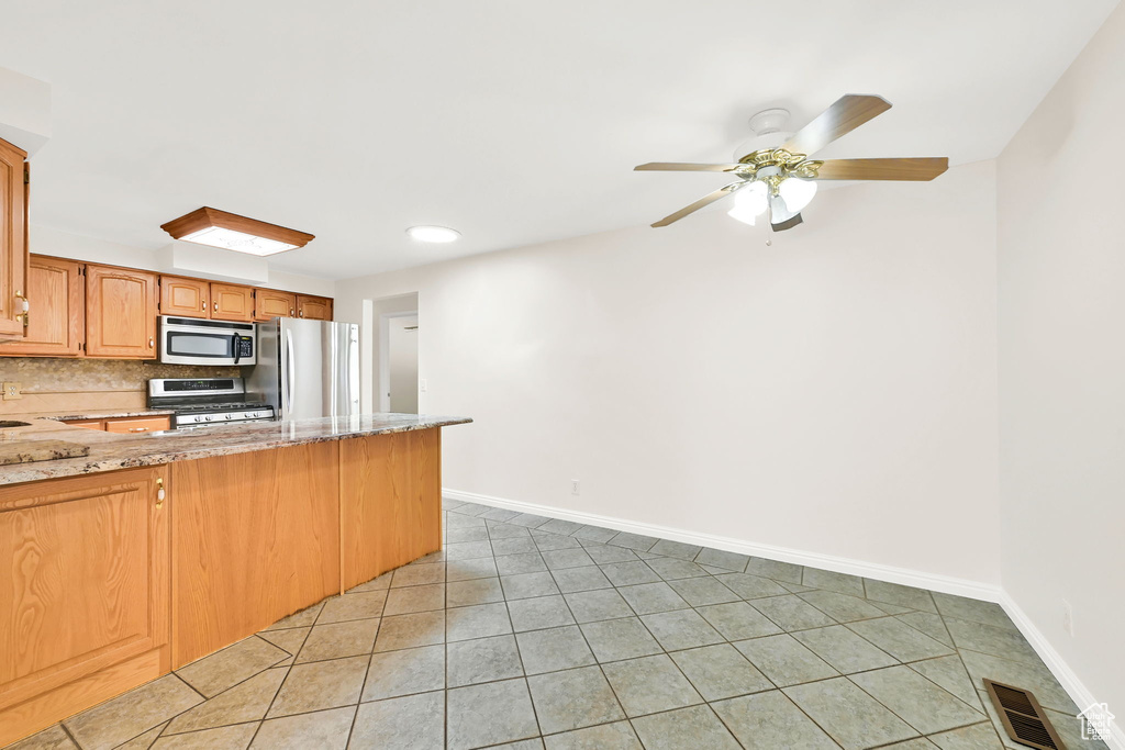Kitchen featuring stainless steel appliances, light tile patterned flooring, a peninsula, tasteful backsplash, and baseboards