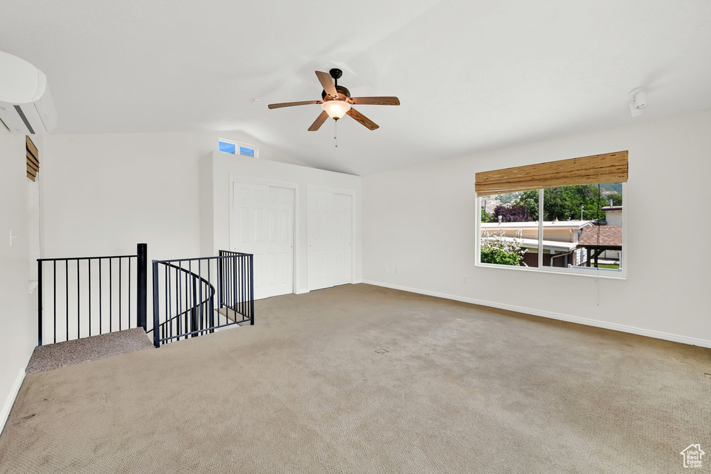 Carpeted empty room featuring lofted ceiling, a wall mounted air conditioner, baseboards, and a ceiling fan