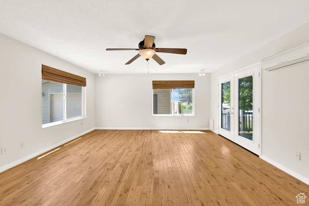 Unfurnished room featuring ceiling fan, baseboards, light wood-style flooring, and a wall mounted air conditioner