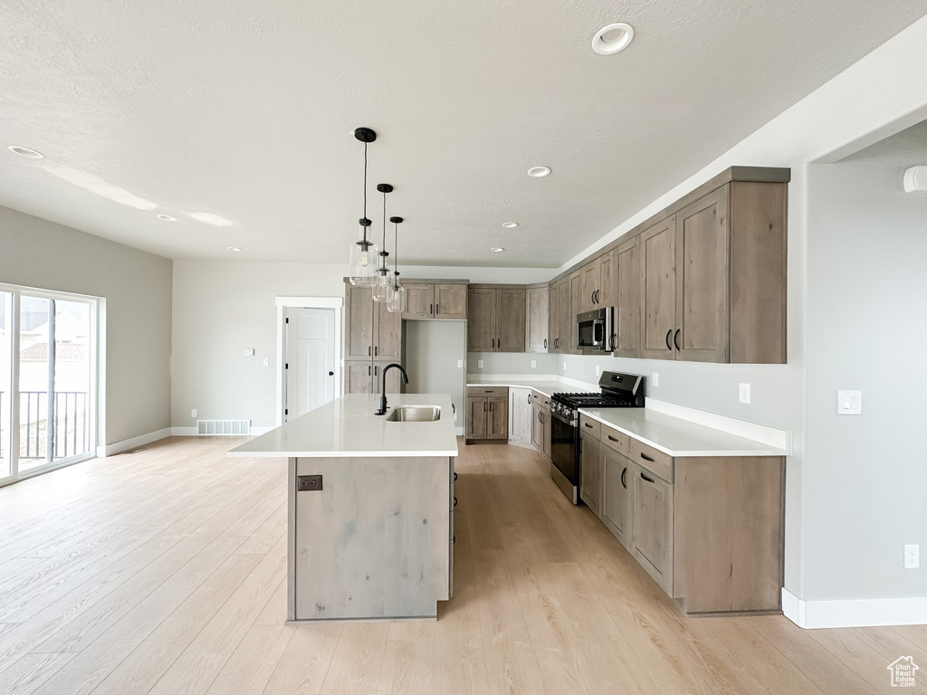 Kitchen with light countertops, hanging light fixtures, appliances with stainless steel finishes, a sink, and an island with sink