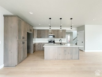 Kitchen with stainless steel appliances, light countertops, a center island with sink, and hanging light fixtures