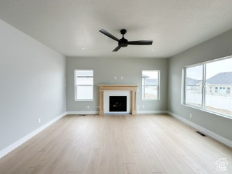Unfurnished living room with light wood finished floors, a fireplace, a ceiling fan, and baseboards