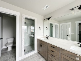 Bathroom featuring double vanity, visible vents, toilet, a sink, and a shower stall