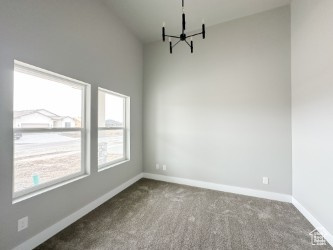 Empty room with carpet floors, a notable chandelier, and baseboards