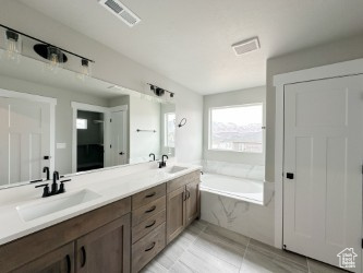 Full bathroom with double vanity, visible vents, a sink, and a bath