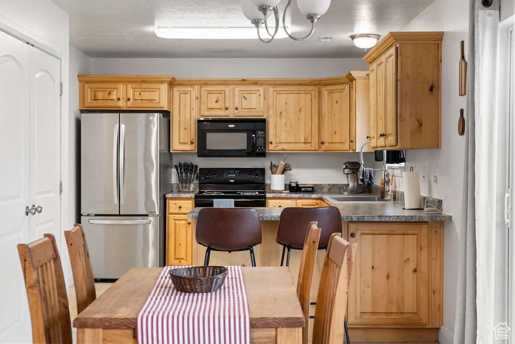 Kitchen featuring light brown cabinetry, sink, a notable chandelier, and black appliances