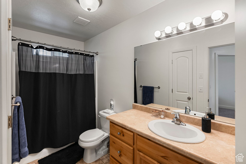 Bathroom with vanity, curtained shower, toilet, and a textured ceiling