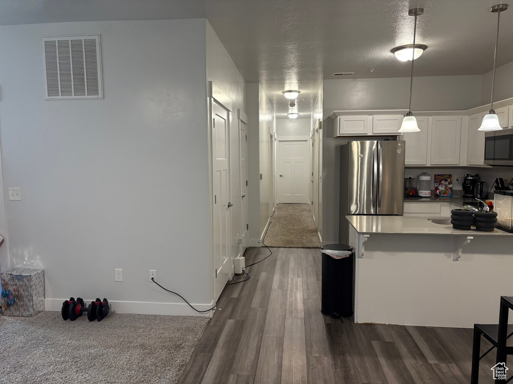 Kitchen with appliances with stainless steel finishes, dark hardwood / wood-style flooring, a breakfast bar, decorative light fixtures, and white cabinets