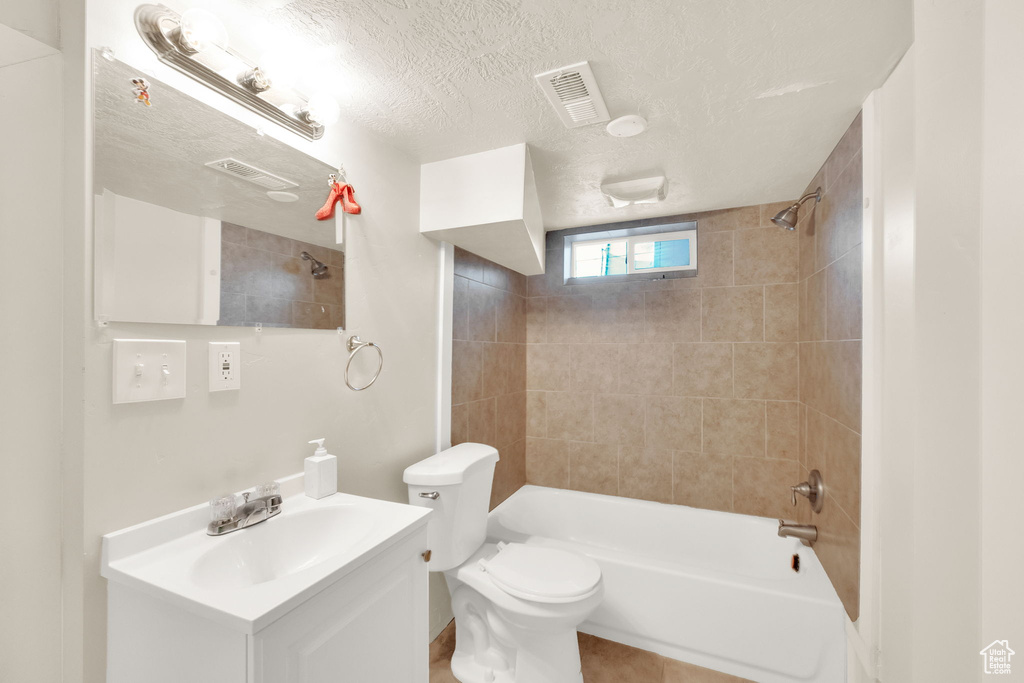 Full bathroom featuring vanity, a textured ceiling, tiled shower / bath combo, and toilet