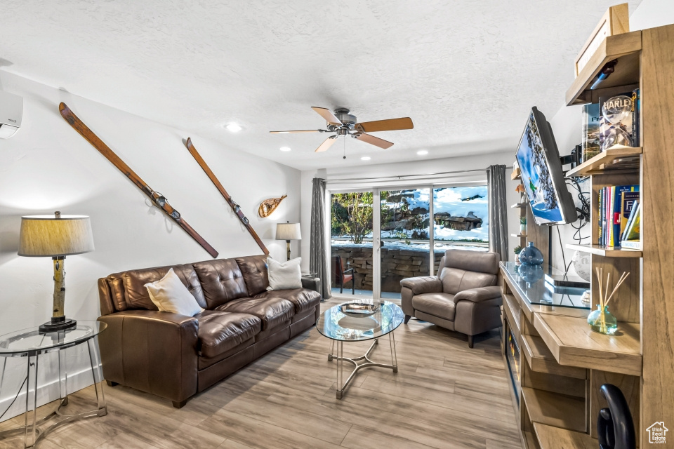 Living room with a textured ceiling, light wood-type flooring, and ceiling fan