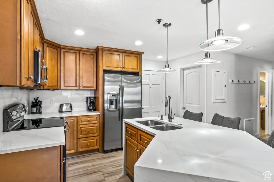 Kitchen with sink, stainless steel appliances, light stone counters, an island with sink, and light wood-type flooring