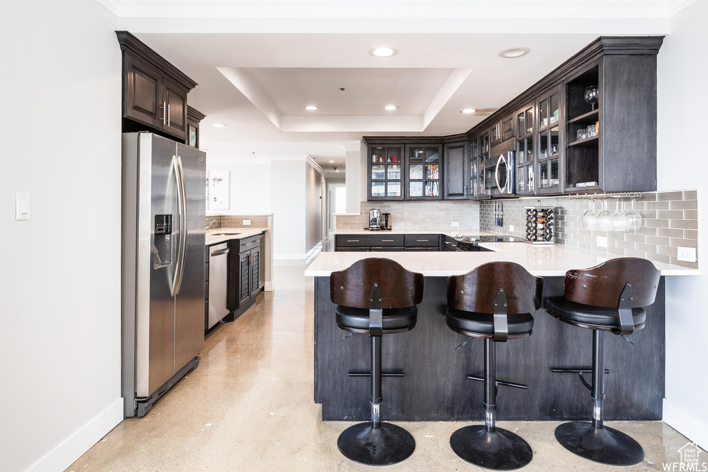 Kitchen featuring backsplash, a kitchen breakfast bar, appliances with stainless steel finishes, a tray ceiling, and kitchen peninsula