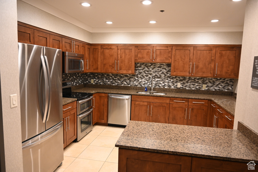 Kitchen featuring decorative backsplash, stainless steel appliances, sink, dark stone countertops, and light tile patterned flooring