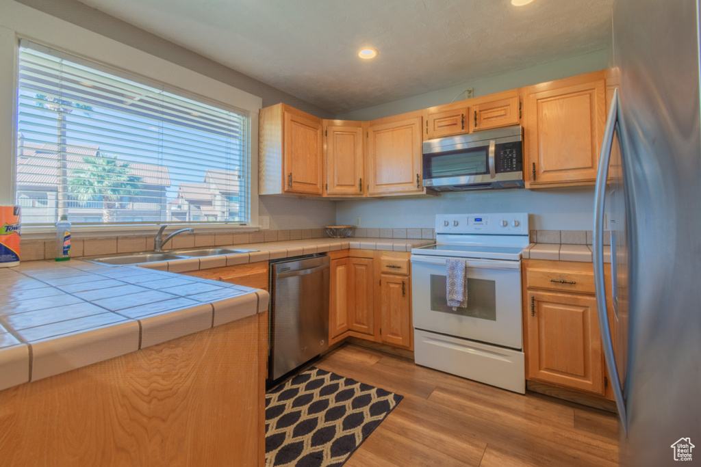 Kitchen featuring tile counters, sink, stainless steel appliances, light brown cabinetry, and light wood-type flooring