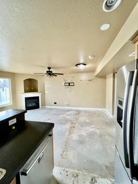 Unfurnished living room featuring unfinished concrete flooring, a textured ceiling, ceiling fan, and a fireplace