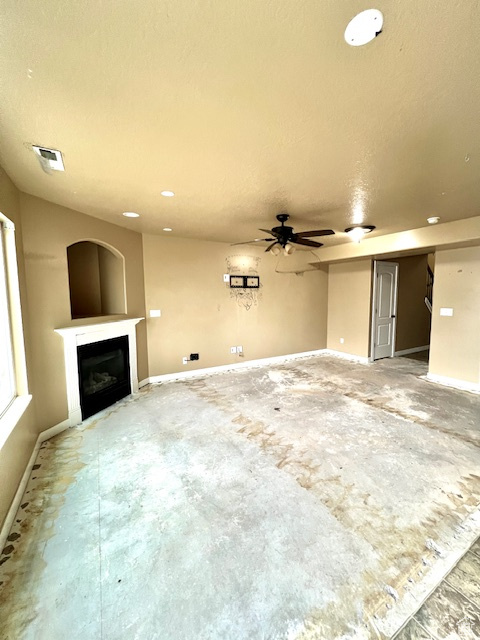 Unfurnished living room featuring visible vents, baseboards, a glass covered fireplace, and a ceiling fan