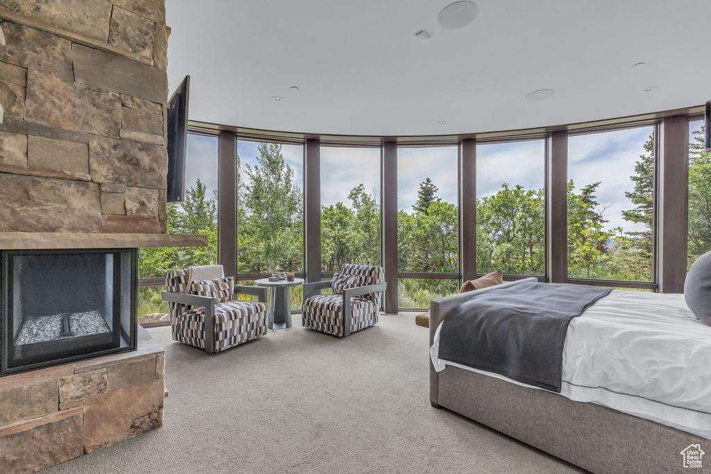 Carpeted bedroom featuring a wall of windows and a stone fireplace