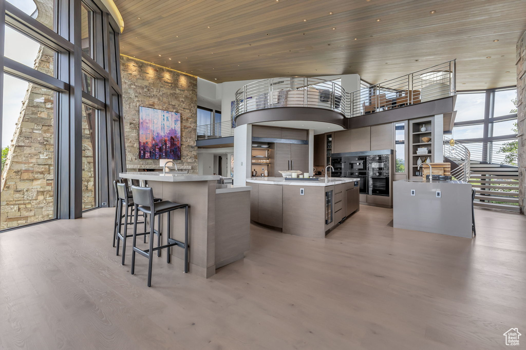 Kitchen with a kitchen island with sink, a high ceiling, wooden ceiling, light wood-type flooring, and light countertops