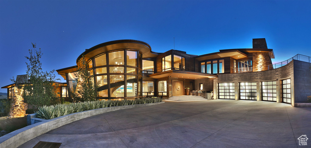 View of front facade featuring driveway, a balcony, an attached garage, and a chimney
