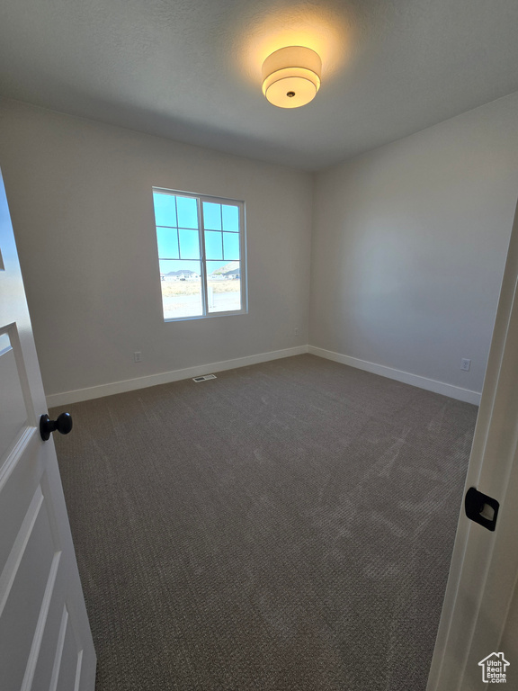 Empty room with visible vents, baseboards, and dark carpet