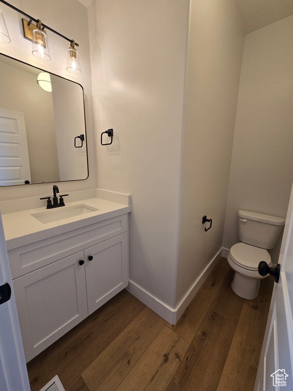 Half bath with baseboards, vanity, toilet, and wood finished floors