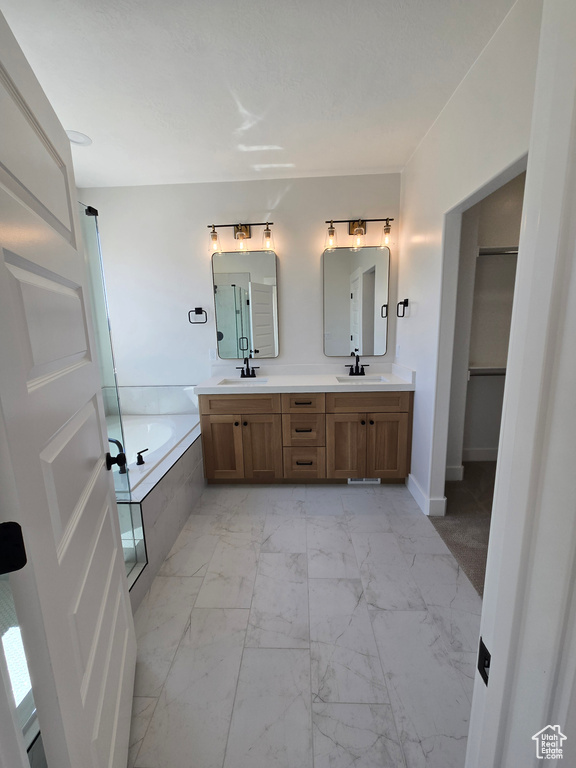 Full bath featuring marble finish floor, a bath, double vanity, and a sink